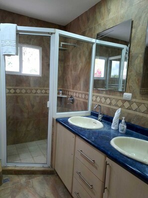 Een badkamer met twee wastafels, een douche met glazen deur, een grote spiegel en een betegelde spatwand.