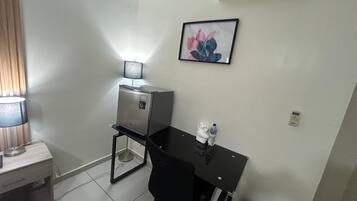 A small office space with a desk, chair, a lamp, a water bottle, a trash bin, and a framed picture on the wall.