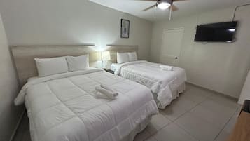 Een hotelkamer met twee bedden, een plafondventilator, een aan de muur bevestigde televisie en een ingelijst schilderij.