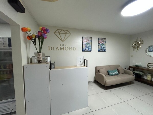 A reception area with a white reception desk, a beige sofa, and wall art including a diamond logo and floral paintings. - The Diamond Hotel (San Salvador)