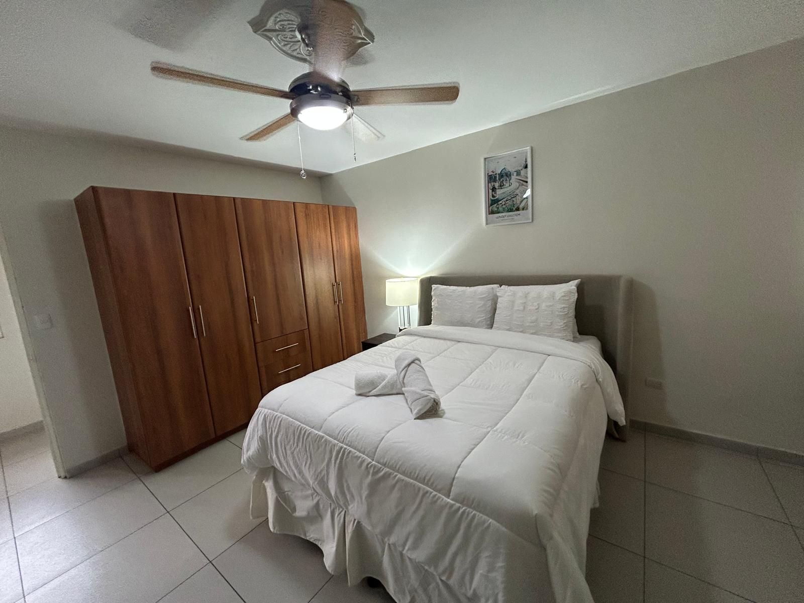A bedroom with a bed, a wardrobe, a ceiling fan, and a wall-mounted lamp.