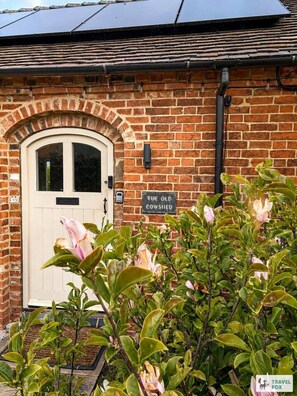 A brick building with a white door, a sign reading 'The Old Cowshed,' and a solar panel on the roof. - The Old Cowshed - with free parking! (Marchington)