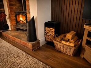 A cozy room with a fireplace, a wood stove, and a stack of firewood. - The Old Cowshed - with free parking! (Marchington)