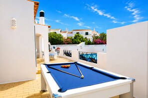 Un tavolo da biliardo con vista libera sugli spazi circostanti, tra cui un patio con sedie e un tavolo, e un edificio sullo sfondo con balconi e fiori.