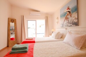 Ein Hotelzimmer mit zwei Betten, einem großen Spiegel, einem Gemälde und Blick durch das Fenster.