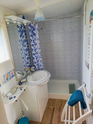 Un baño con lavamanos blanco, espejo, cortina de ducha y toallero.