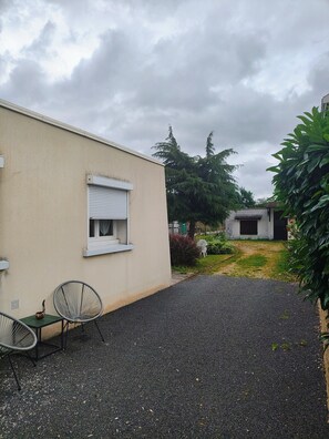 Un edificio con fachada blanca, una ventana con persiana blanca y un camino de entrada de grava.