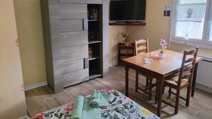 Quarto com armário de madeira, televisão fixada na parede, mesa de jantar com cadeiras e janela com cortina.