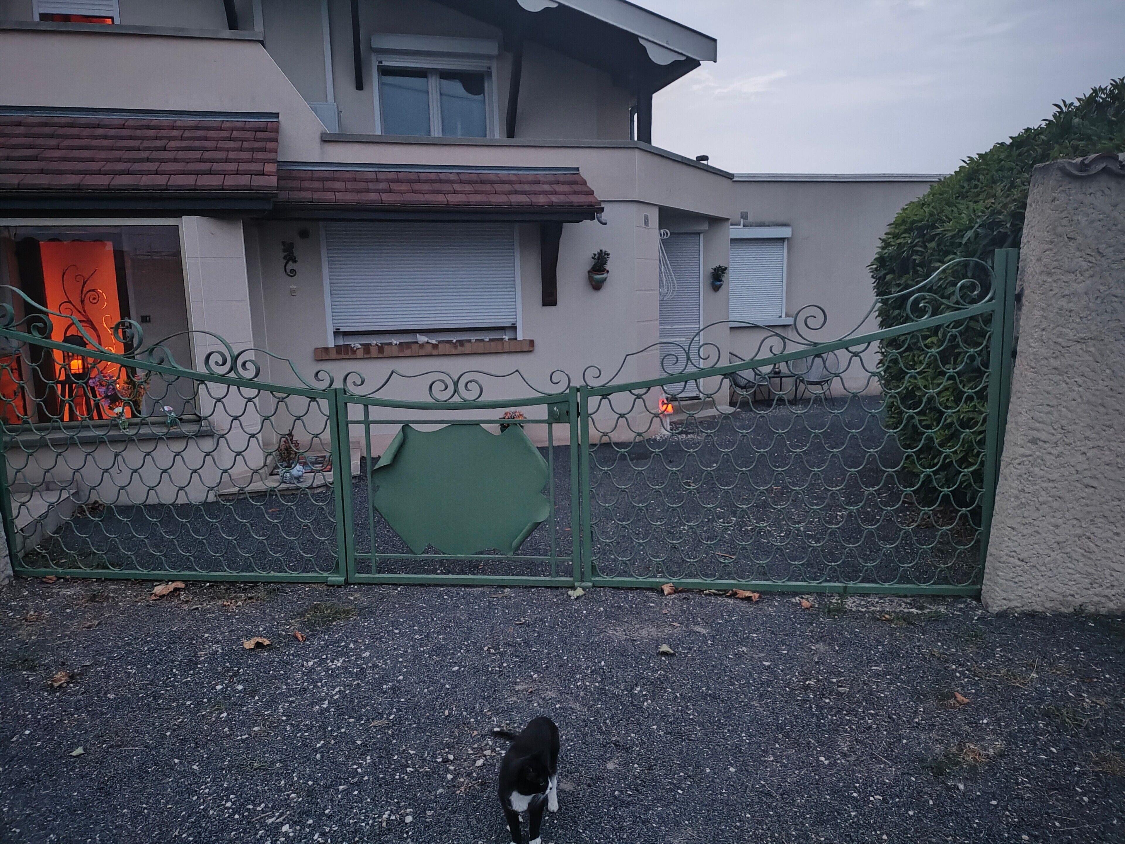 A residential building with a gated entrance, a paved driveway, and a visible garage door.