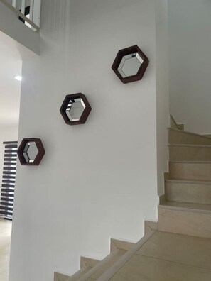 A staircase with a handrail, a white wall with three hexagonal mirrors, and a spiral staircase to the left. - Beautiful house 2 bedroom wifi tv (Caucel)
