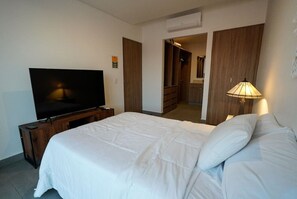 Ein Hotelzimmer mit Bett, Fernseher, Lampe, Kleiderschrank und einem sichtbaren Badezimmer durch eine offene Tür.