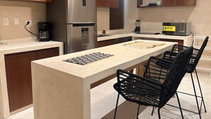Une cuisine moderne dotée d’un îlot central, d’appareils électroménagers en acier inoxydable et de chaises noires en osier tressé.