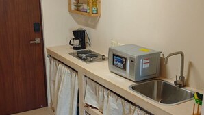 Een kleine kitchenette met een magnetron, koffiezetapparaat en een spoelbak.