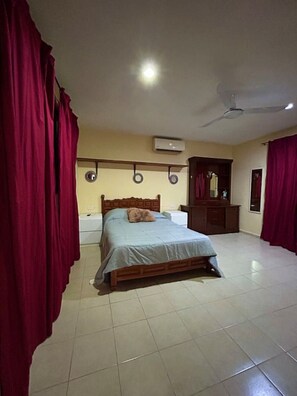 A bedroom with a bed, a ceiling fan, an air conditioning unit, and a wooden wardrobe. - Departamento en Xcumpich 2 Recamaras (Merida)