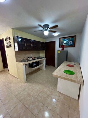 A compact kitchen with a ceiling fan, dark cabinets, a small island, and a tiled floor. - Departamento en Xcumpich 2 Recamaras (Merida)