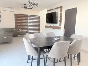 A dining area with a table and chairs, a sofa, a TV mounted on the wall, and a door. - Casa 5 minutos del Foro GNP Américas (Mérida)