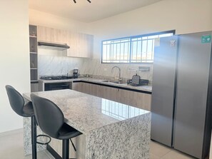 A modern kitchen with a marble island, stainless steel appliances, and a large window. - Casa 5 minutos del Foro GNP Américas (Mérida)