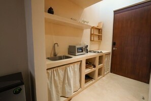 Eine kompakte Küchenzeile mit Spüle, Toaster und Mikrowelle. Eine Holztür und ein Regal mit Gläsern sind ebenfalls vorhanden.