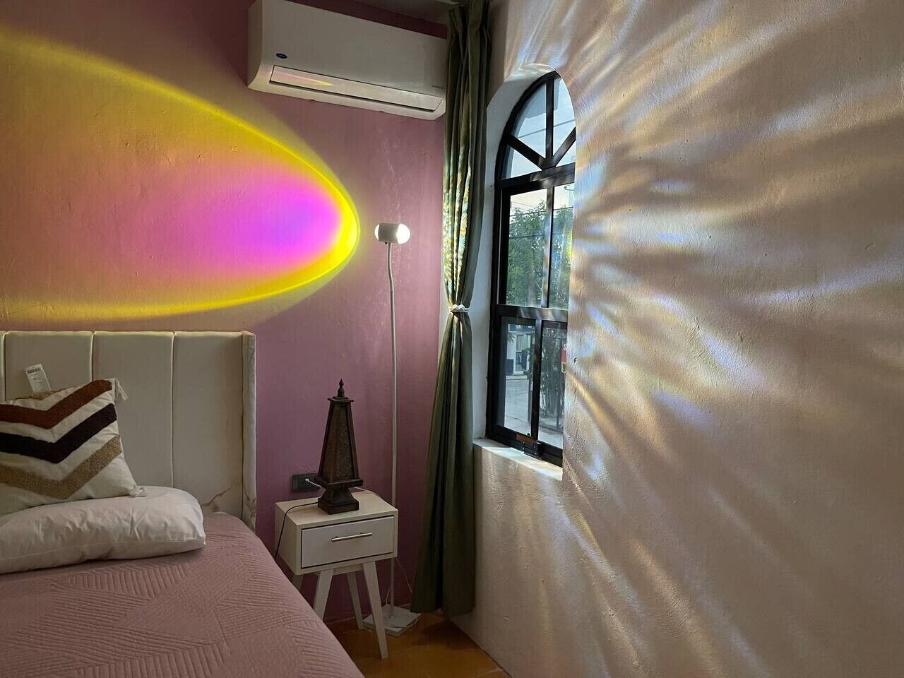 A bedroom with a bed, bedside table, lamp, and window.