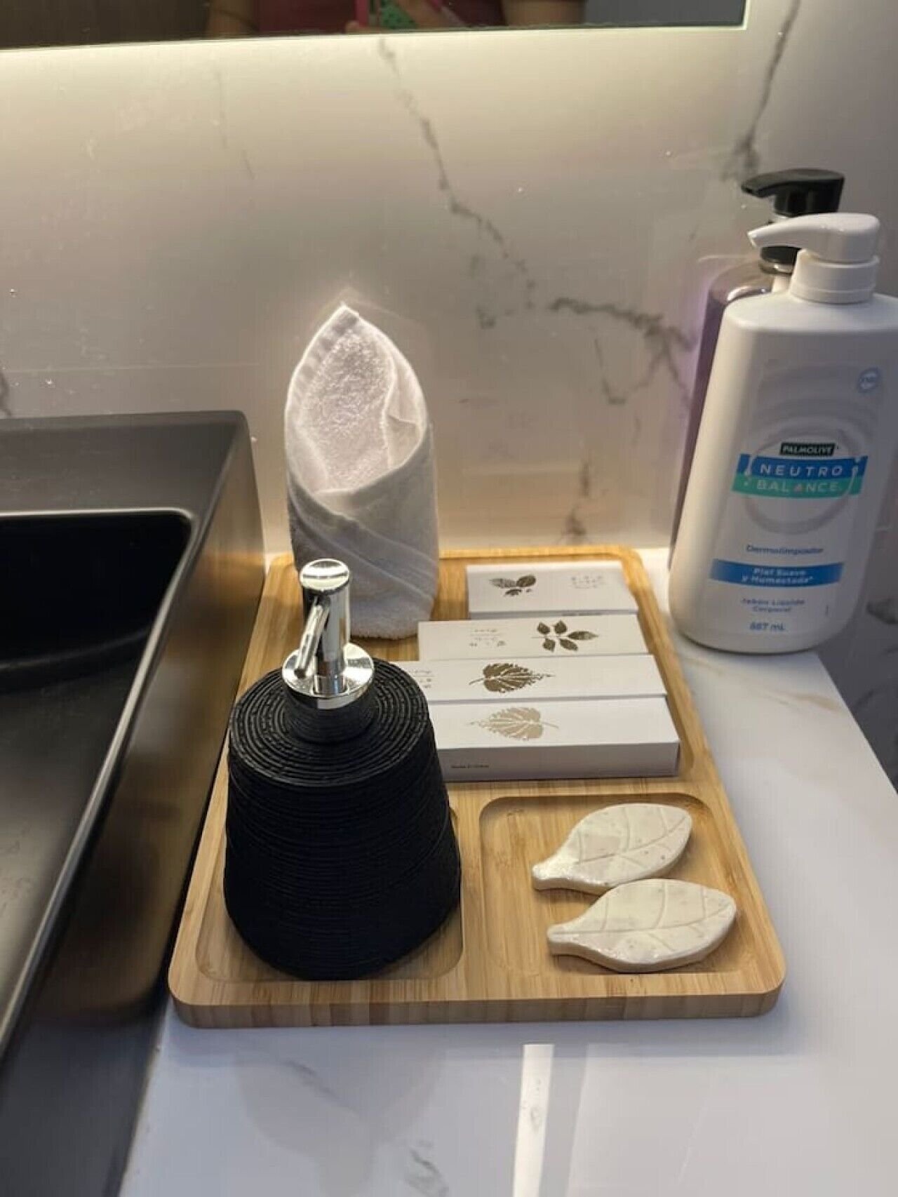 A kitchen counter with a marble backsplash, a black kitchen tool, a white towel, a bottle of hand soap, and some soap boxes.