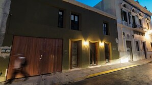 Vista de una calle con un edificio que tiene una puerta de madera grande, varias ventanas y un balcón con barandillas.