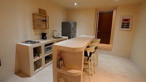Una cocina compacta con refrigerador integrado, cafetera y un pequeño comedor con taburetes.