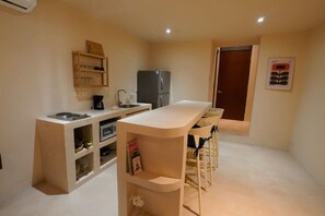Eine kompakte Küche mit Einbaukühlschrank, einer Kaffeemaschine und einer kleinen Essecke mit Hockern.