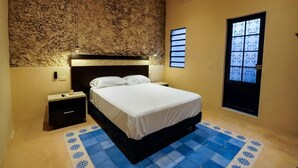 Un dormitorio con pared de piedra, cama, mesita de noche, ventana y puerta.