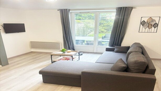 Ein modernes Wohnzimmer mit einem Ecksofa, einem Flachbildfernseher und einem großen Fenster mit Vorhängen.