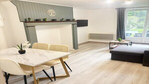 Ein modernes Wohnzimmer mit Essbereich, einer Couch, einem an der Wand befestigten Fernseher und einem Fenster mit Vorhängen.