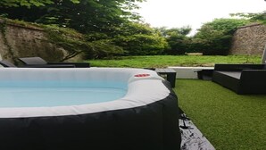 Ein aufblasbarer Pool mit weißem Rand, umgeben von künstlichem Rasen und Gartenmöbeln.