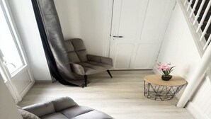 Ein Zimmer mit einer grauen Couch, einem kleinen runden Tisch mit einer Pflanze und einer weißen Tür.