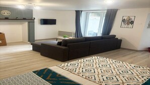 Ein modernes Wohnzimmer mit einer Couch, einem gemusterten Teppich, einem Flachbildfernseher und einem Fenster mit Vorhängen.