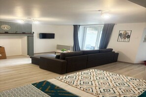 Uma sala de estar moderna com um sofá, um tapete estampado, uma televisão de tela plana e uma janela com cortinas.