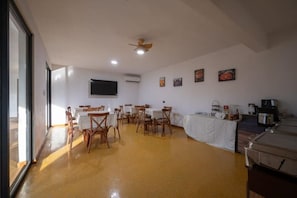 Ein Essbereich mit Tischen und Stühlen, einem Deckenventilator, einem Fernseher und einer Küchenzeile mit Geräten.