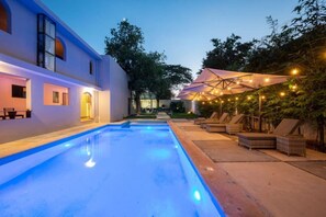 A swimming pool with a blue-lit edge, lounge chairs, and umbrellas under string lights. - Suite Estrella India (Merida)