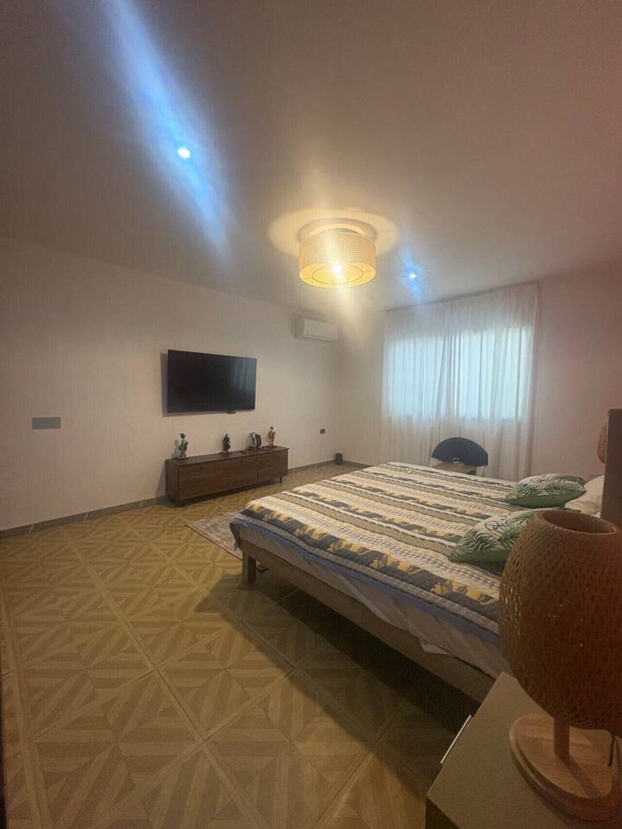 Een slaapkamer met een bed, een televisie, een dressoir en een lamp.