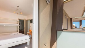 A hotel room with a bunk bed, a small table, a chair, a mirror, and a view of the outside. - B&B Acquamarina - Quadrupla (Gallipoli)