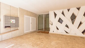 Un interior moderno con mostrador de recepción, buzones, puerta corredera de cristal y diseño geométrico en la pared.