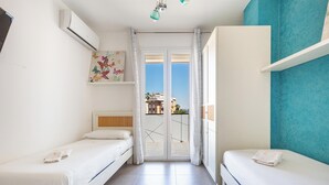 Una habitación con dos camas, una ventana con cortinas, aire acondicionado instalado en la pared y vistas a edificios.