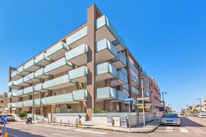 A multi-story building with balconies, a clear sky, and a street with cars and a pedestrian crossing. - B&B Acquamarina - Doppia (Gallipoli)