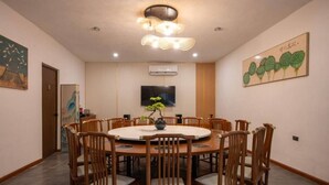 Un salón de conferencias con una mesa redonda, sillas de madera, una planta en maceta, un televisor de pantalla plana y obras de arte en las paredes.