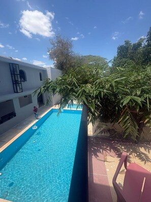 A rectangular pool with clear blue water, surrounded by a white building with arched windows and a red chair. - Suite Estrella Mongolia (Merida)