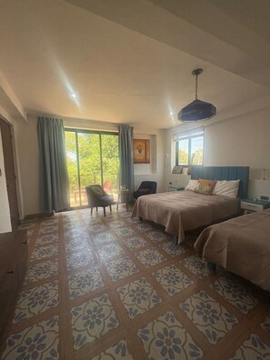 Ein Schlafzimmer mit zwei Betten, einem Sessel, einem Tisch und einem großen Fenster mit Vorhängen.