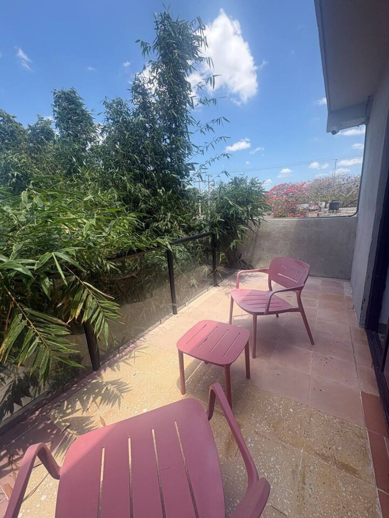 A balcony with two pink chairs, a metal railing, and a view of trees and a building.