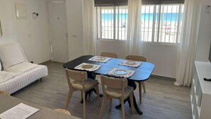 A room with a bed, a dining table with chairs, a window with a view of the beach, and a door. - Córdoba 8 by 7Escalones (Rota)