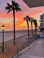 Un paseo marítimo con palmeras, un farol y un edificio con balcón.