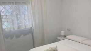A room with a bed, a nightstand, a window with curtains, and a tiled floor. - Córdoba 8 by 7Escalones (Rota)