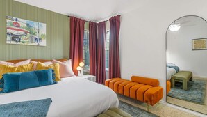 Una habitación de hotel con una cama, una mesita de noche, un espejo y una ventana con cortinas.