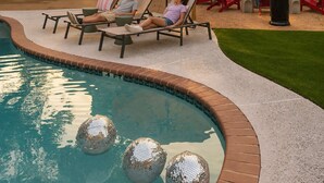 Una piscina con sillones de descanso y un pequeño jardín.
